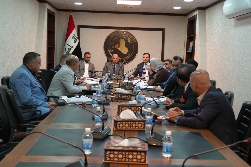 694606539_1302135375353191_3057366281023105541_n - مرصد تشريع Group of officials seated around a long conference table in a formal meeting room, Iraqi flag in the background.